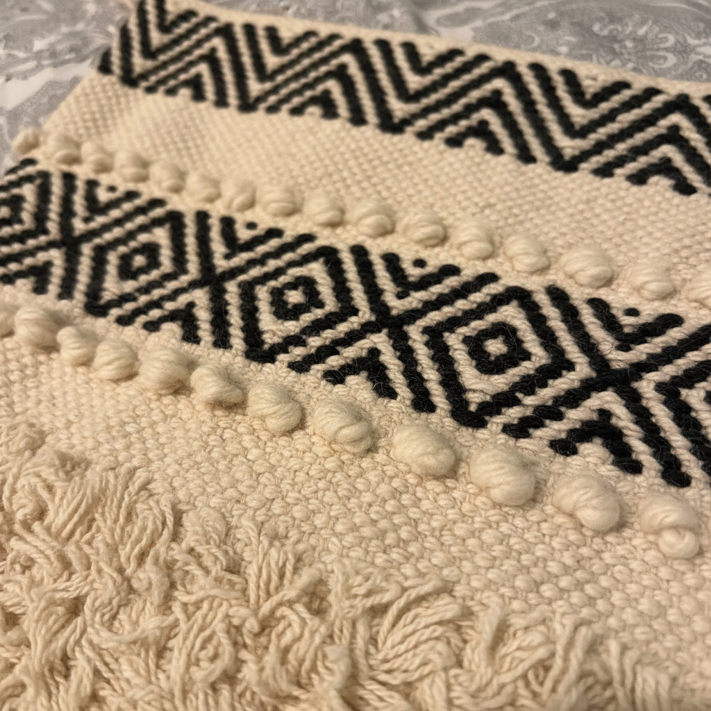 Close-up detail of ivory black geometric chevron weave, bobble trim and fringe texture