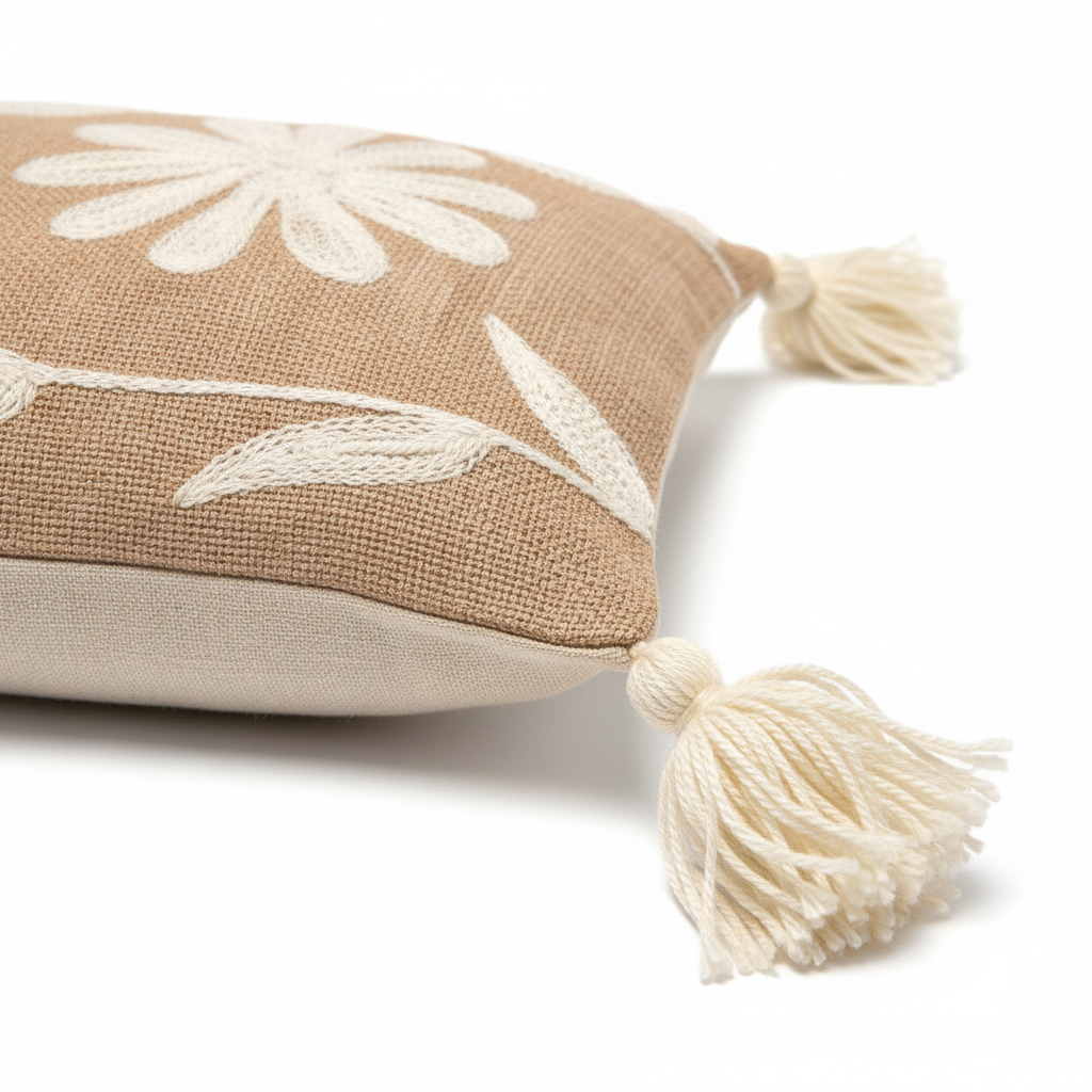 Close-up of white daisy floral embroidery on sandy beige linen with tassel detail